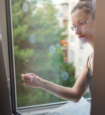 Frau klebt Aufkleber für Vögel an Fenster. Diese Aufkleber haben eine spezielle Beschichtung, die ultraviolettes Sonnenlicht reflektiert und so verhindert, dass Wildvögel versehentlich gegen Fenster fliegen.