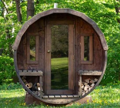 Kleine Fasssauna aus dunkel gebeiztem Holz mit Glastür un zwei Fenstern.