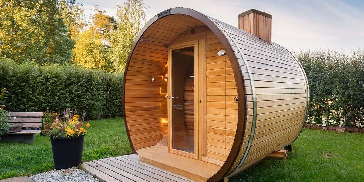 Eine Gartensauna in Form eines Holzfasses aus hellem Holz, in einem gepflegten Garten eines Einfamilienhauses.