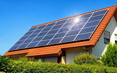 Strahlend blauer Himmel über einem Hausdach mit roten Ziegeln und Solarmodulen