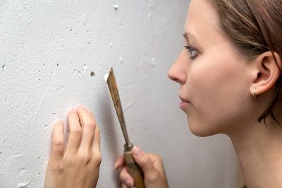 Junge Frau untersucht die Wand auf Löcher und verschließt diese mit Spachtelmasse