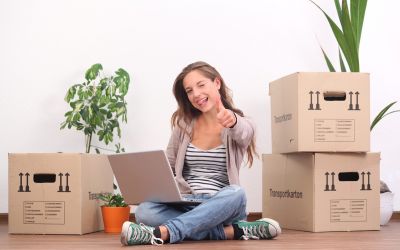 Studentin sitzt umgeben von Umzugskartons, mit ihrem Notebook auf dem Wohnzimmerboden