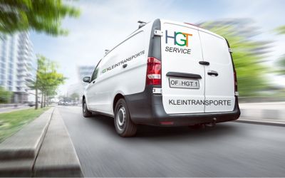 Weißer Transporter mit Werbeaufschrift fährt zügig durch die Stadt