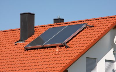 Blauer Himmel über Dach mit roten Ziegeln und zwei auf dem Dach befestigten Solarthermie-Modulen