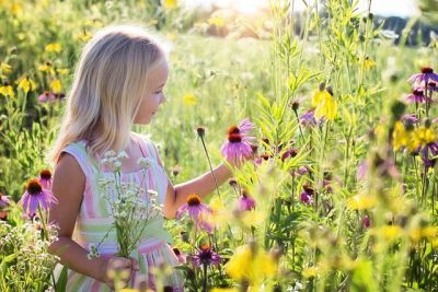 Ein Mädchen steht in einer Wildblumenwiese und bewundert die Blütenpracht.