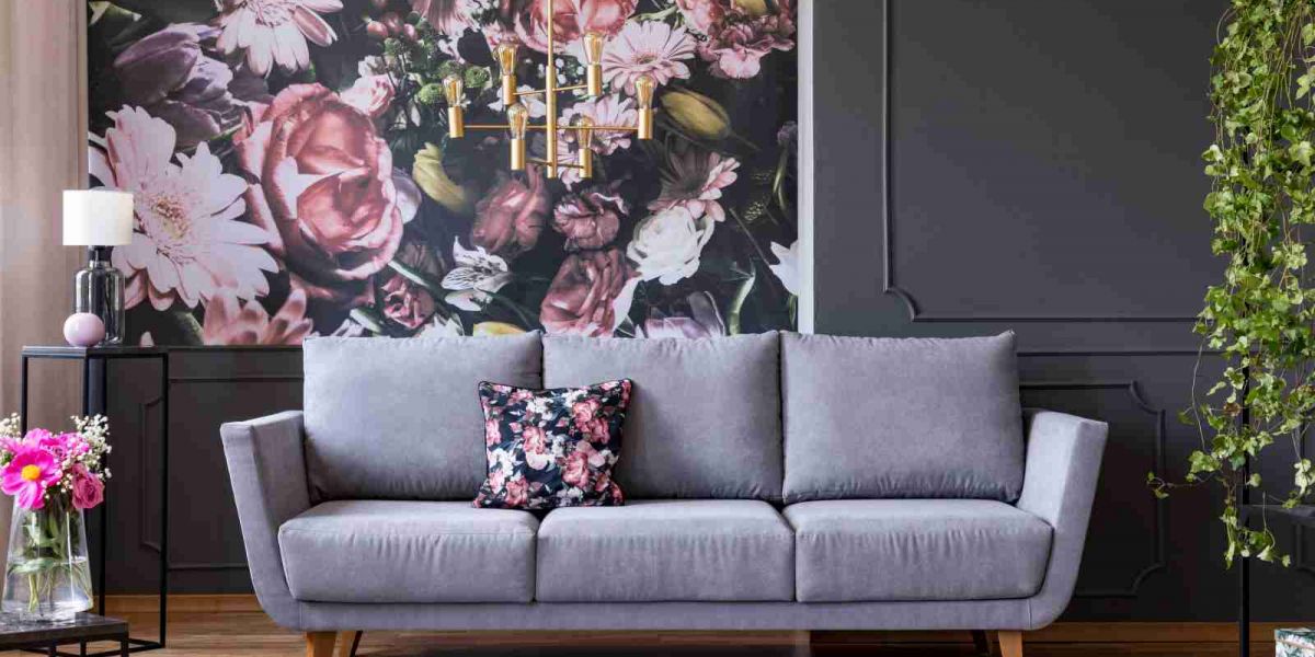 Wonzimmerwand mit Tapete im Blumendekor, davor ein graues Sofa und ein kleiner Tisch