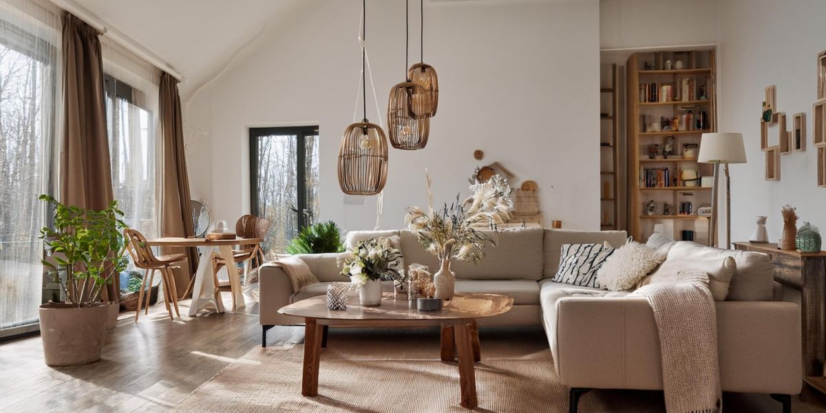 Gemütlich eingerichtetes Wohnzimmer mit beiger Couch, Korblampen, braunem Couchtisch und vielen Dekoelemten