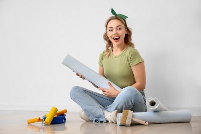 Junge Frau sitzt auf den Fußboden und kontrolliert Ihre benötigten Werkzeuge zum tapezieren