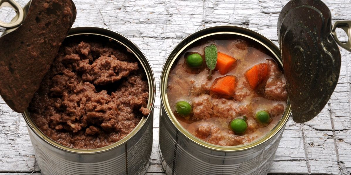 Zwei Dosen mit Nassfutter auf einem Holztisch stehend. Eine Dose nur Fleisch, die andere Dose enthält Fleisch und Gemüse.